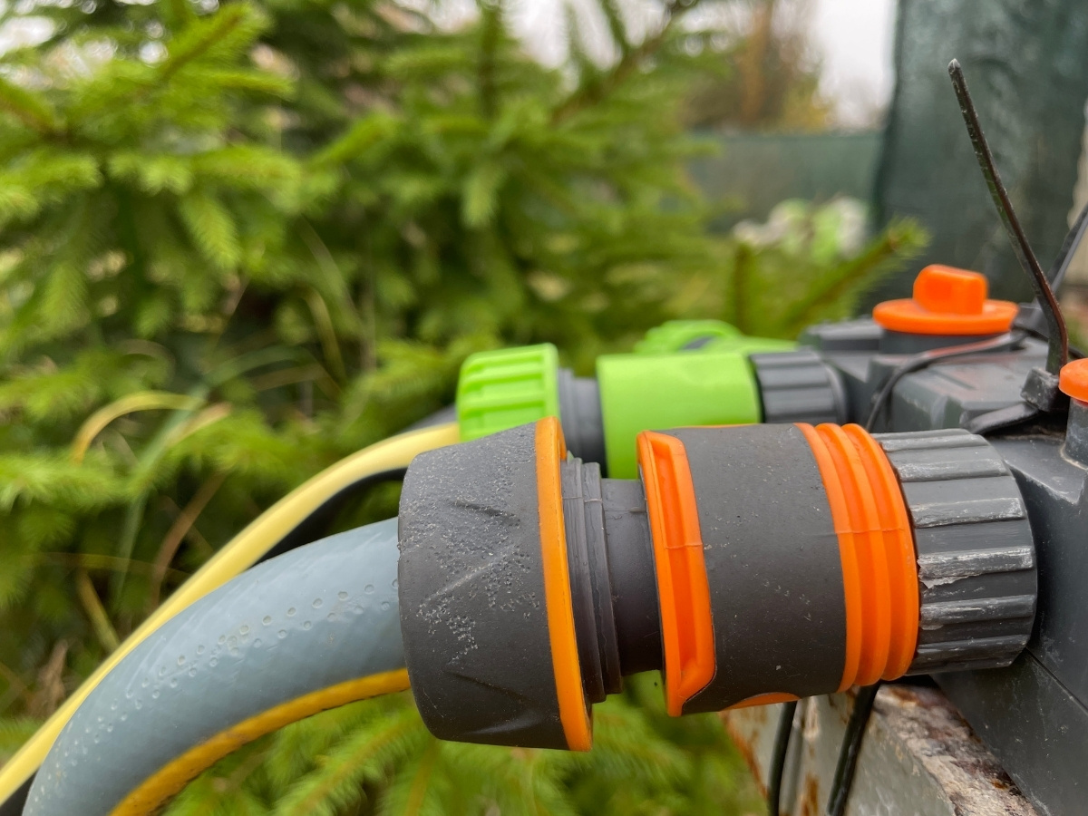 Nahaufnahme eines Gartenschlauchs mit orangefarbenen und grauen Verbindungsstücken an einer Bewässerungsanlage