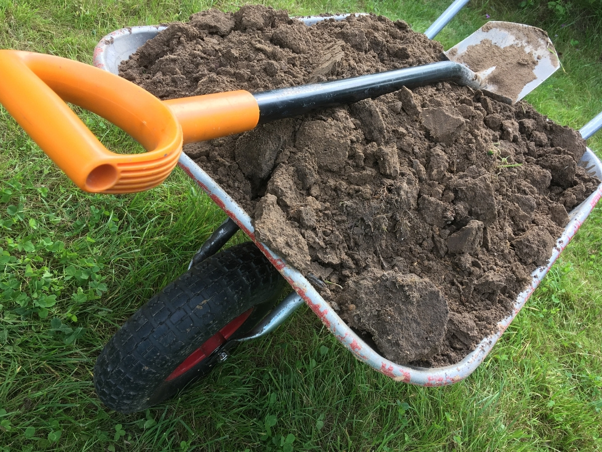 Schubkarre mit orangefarbenem Griff, gefüllt mit Erde, auf Grasboden