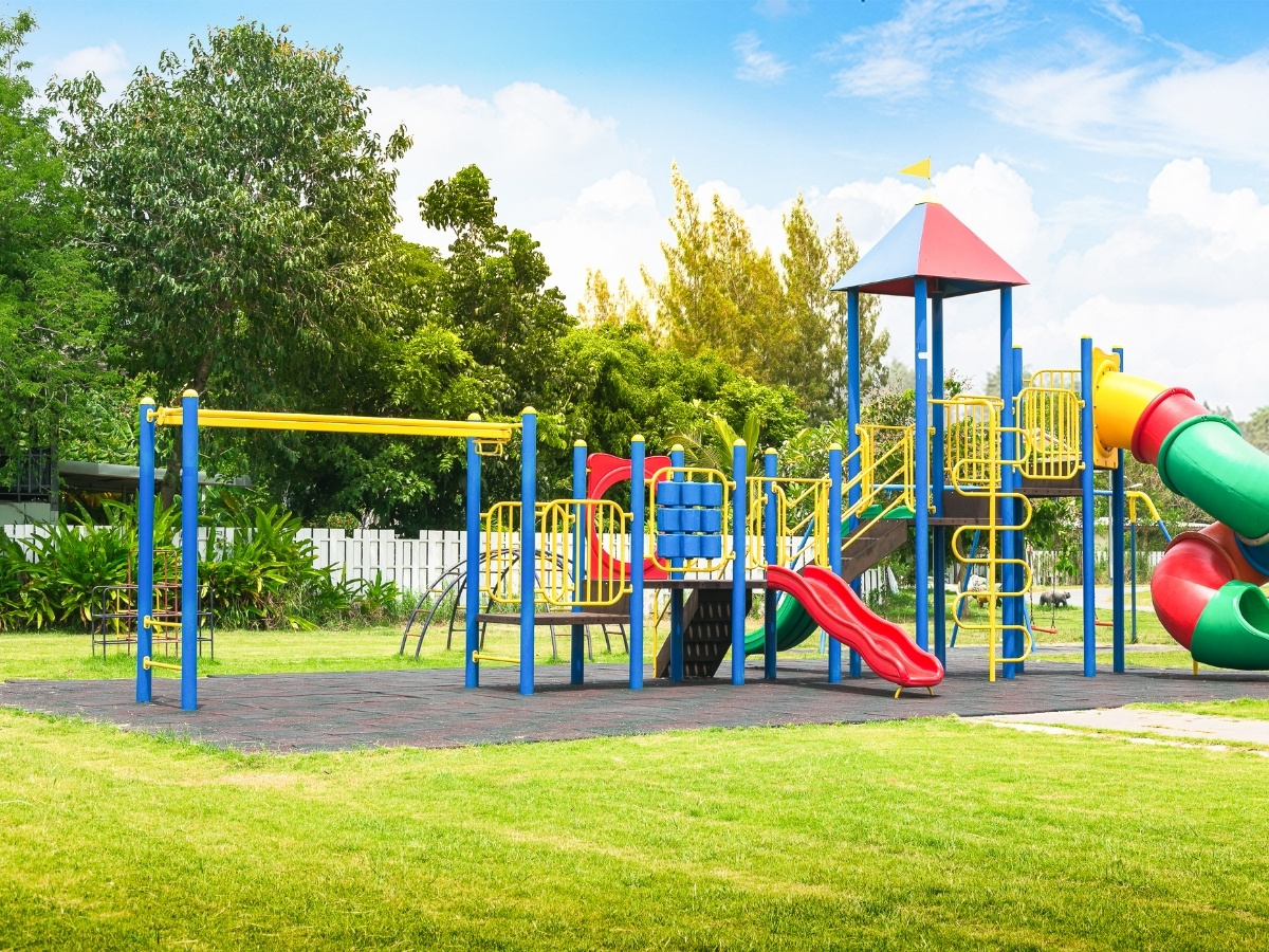 Bunter Spielplatz mit Rutsche, Klettergerüst und Tunnelrutsche auf grünem Rasen unter blauem Himmel