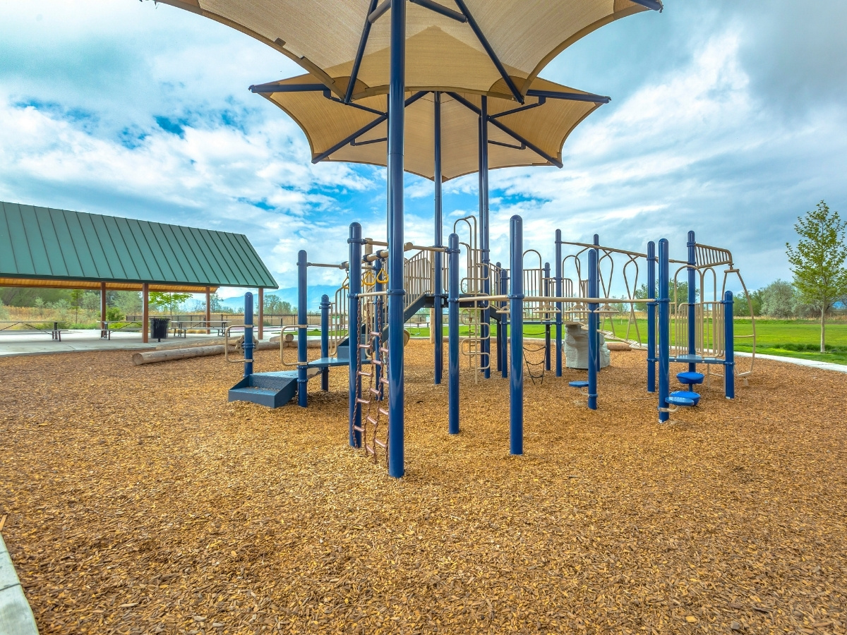 Spielplatz mit Klettergerüst aus blauen Metallstangen und großem Sonnensegel darüber auf Fallschutz aus Holzschnitzeln