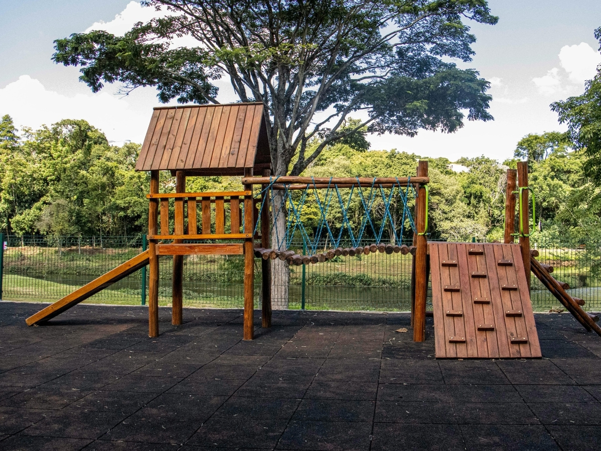 Holz-Klettergerüst mit Rutsche, Hängebrücke und Kletterwand auf Fallschutz Boden vor Bäumen