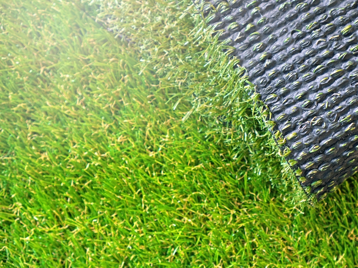 Nahaufnahme von grünem Rollrasen, der an einer Kante aufgerollt ist und eine schwarze Kunststoffunterlage zeigt